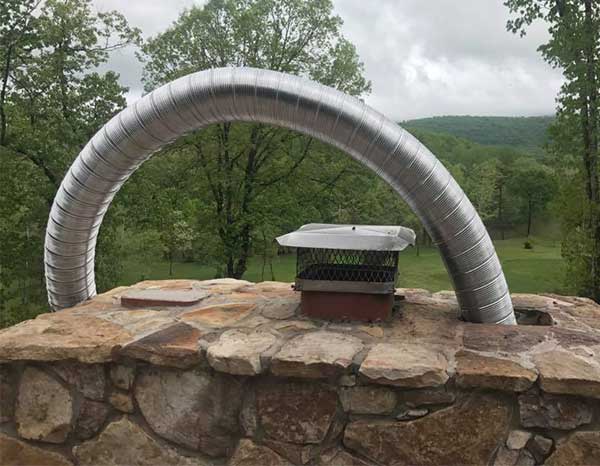 Stainless Steel Liner being installed in a rock chimney with mountains and trees in the background.